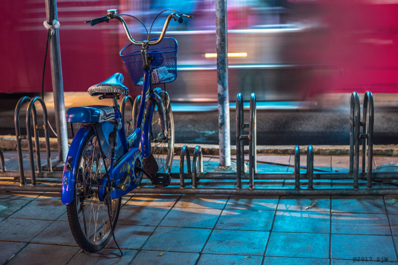 Bicycle in a stand as a bus passes by.